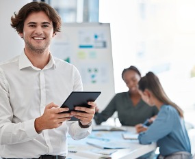 A young man smiles and holds an iPad while performing Website Design in East Peoria IL